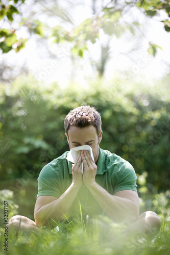 Photo: A young man sitting on the grass, blowing his nose A young man sitting on the grass, blowing his nose