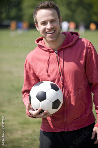 Photo: A young man standing in the park, holding a football A young man standing in the park, holding a football