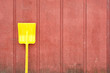 Yellow toy shovel against red barn wall Yellow toy shovel against red barn wall