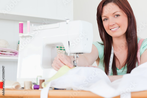 Photo: Beautiful red-haired female sewing in the living room Beautiful red-haired female sewing in the living room