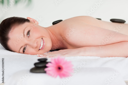 Foto: Happy young woman with massage stones and a pink gerbera Happy young woman with massage stones and a pink gerbera