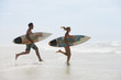 Couple with surfboards running on beach