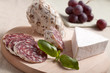 Traditional sliced salami on wooden board with brie, grapes, bas