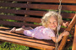 Photo: Cute little girl with blond curly hair playing on wooden chain s Cute little girl with blond curly hair playing on wooden chain s