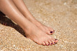 Woman feet with dark pedicure relaxing on the sand