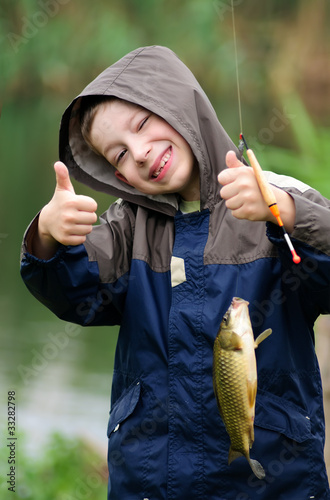 Foto: Cute young boy with great smile holding carp and show thumb up Cute young boy with great smile holding carp and show thumb up