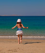 The little girl in a white skirt runs across the sand to the sea