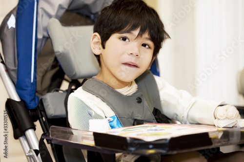 Photo: Disabled four year old boy studying or reading in wheelchair Disabled four year old boy studying or reading in wheelchair