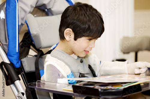 Photo: Disabled four year old boy studying or reading in wheelchair Disabled four year old boy studying or reading in wheelchair
