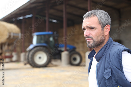 Photo: Farmer standing in front of a barn containing a tractor Farmer standing in front of a barn containing a tractor