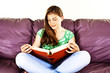 Portrait of a young woman reading cross-legged on a sofa
