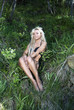 blonde girl in a black bathing suit sitting in the forest