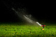 Foto: lawn sprinkler spraying water over green grass at night lawn sprinkler spraying water over green grass at night