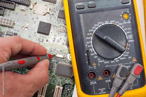 Photo: Engineer examining motherboard by multimeter Engineer examining motherboard by multimeter