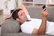 Amused man lying on the sofa sending a text message
