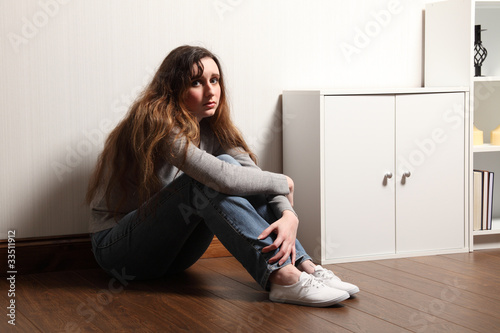 Photo: Nervous frightened young girl sits alone on floor Nervous frightened young girl sits alone on floor