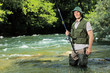 Foto: Young fisherman posing with fishing pole in his hand on a river Young fisherman posing with fishing pole in his hand on a river