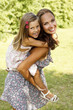 mother giving daughter piggy back ride at summer park