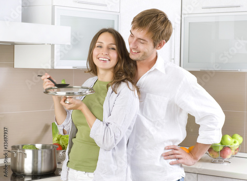 Photo: Young happy couple cooking together at home kitchen Young happy couple cooking together at home kitchen