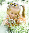 Little girl with magnifying glass looks at flower