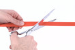 Closeup of a mans hand cutting a red ribbon with scissors