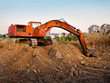 Red construction machine excavating earth near city
