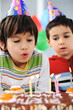 Two little boys blowing candles on cake, happy birthday party