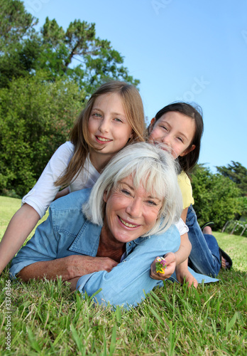 Photo: Senior woman lying down in park with girls on his back Senior woman lying down in park with girls on his back