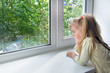 Foto: A sad little girl looks at a pigeon outside the window A sad little girl looks at a pigeon outside the window