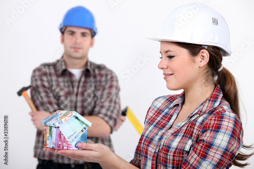 Photo: Female and male construction worker holding house Female and male construction worker holding house