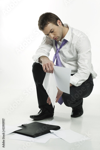 Photo: disappointed young businessman picking up files from the floor disappointed young businessman picking up files from the floor