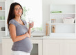 Good looking pregnant woman holding a glass of water while stand