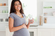 Attractive pregnant woman holding a glass of water while standin