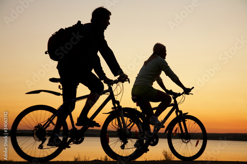 Photo: Young couple riding bicycles at sunset. Young couple riding bicycles at sunset.