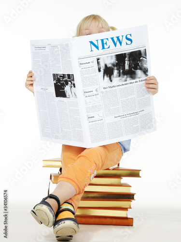 Photo: Little girl seated on books reading newspaper Little girl seated on books reading newspaper