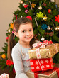 Young child holding gifts in front of Christmas tree