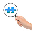 Hand with magnifying glass and puzzle