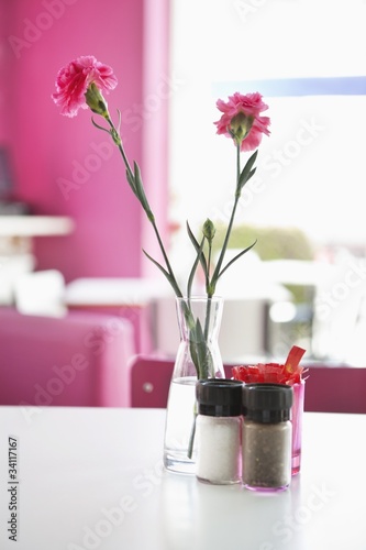 Foto: Vase with pink flowers and salt and pepper shakers on a table in a restaurant Vase with pink flowers and salt and pepper shakers on a table in a restaurant