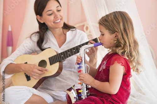 Photo: Woman playing guitar with her daughter playing saxophone Woman playing guitar with her daughter playing saxophone