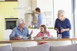 Girl sitting with her parents at a dining table and her father cooking food in the background