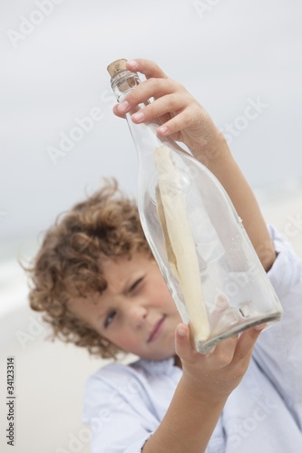 Photo: Boy looking at message in a bottle on beach Boy looking at message in a bottle on beach