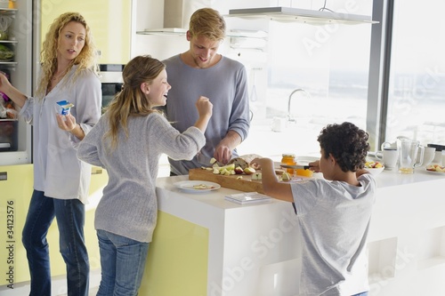 Photo: Couple with their two children preparing food at a domestic kitchen Couple with their two children preparing food at a domestic kitchen