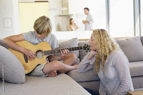 Photo: Teenage boy playing a guitar and his mother listening Teenage boy playing a guitar and his mother listening