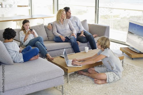 Photo: Couple watching television set while their children busy in different activities Couple watching television set while their children busy in different activities