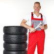 Foto: Smiling motor mechanic standing next to a set of winter tyres Smiling motor mechanic standing next to a set of winter tyres