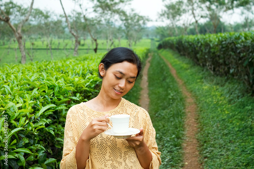 Photo: Ethic young woman drinking healthy tea at tea plantation Ethic young woman drinking healthy tea at tea plantation