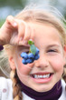 girl holding blueberries in front of her eye smiling