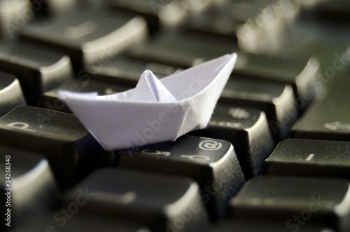 Photo: Origami boat on keyboard -Travel and navigating Internet concept Origami boat on keyboard -Travel and navigating Internet concept