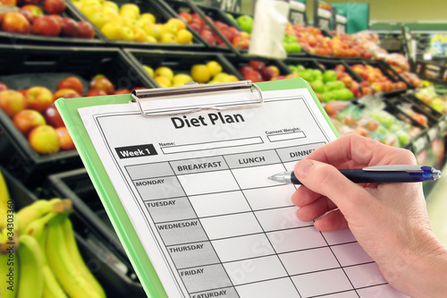 Photo: Hand with Pen Writing a Diet Plan by Supermarket Fruit Hand with Pen Writing a Diet Plan by Supermarket Fruit