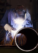 Foto: Worker welding pipe in workshop. Worker welding pipe in workshop.